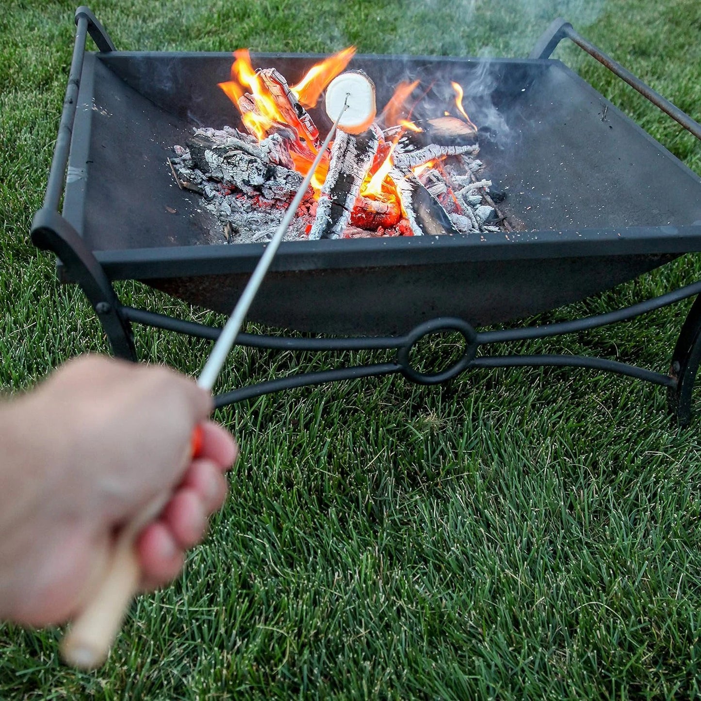 Telescoping s'mores roasting sticks with two prongs, roasting a s'more over a campfire. Perfect for camping and outdoor adventures.
