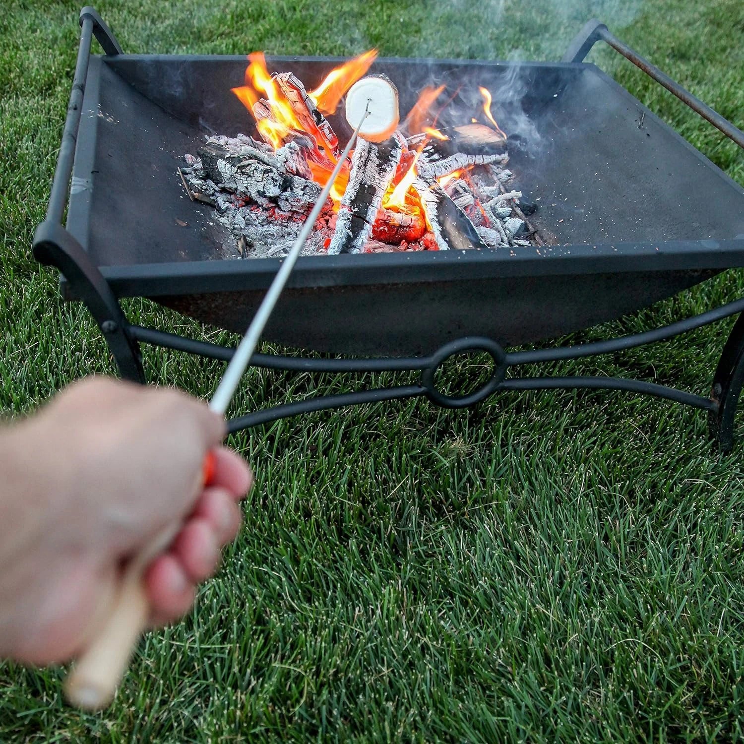Telescoping s'mores roasting sticks with two prongs, roasting a s'more over a campfire. Perfect for camping and outdoor adventures.